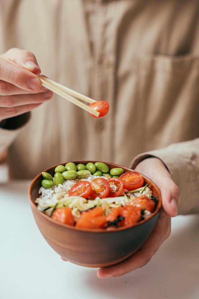person eating a bowl of salad with chopsticks